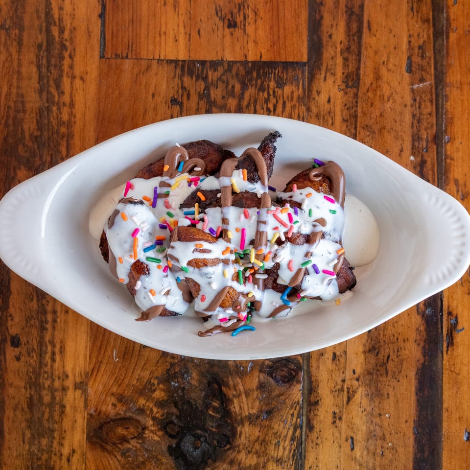 Dessert pastries drizzled with white and chocolate icing and covered in colorful sprinkles on a white platter.